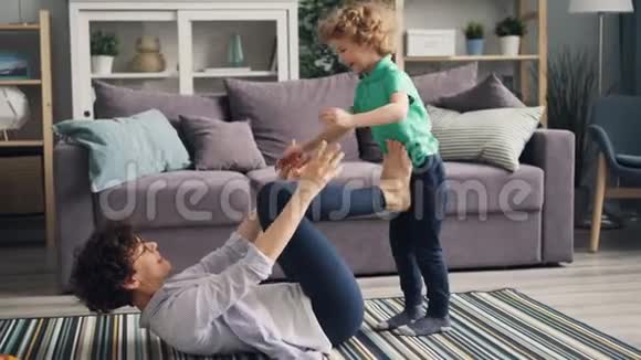 运动妈妈和孩子一起玩用手和腿把他抬起来躺在地板上视频的预览图