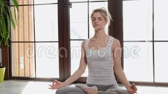 一位年轻漂亮的运动女性金发女郎坐在地板上交叉着双臂呼吸着她的胸部视频的预览图