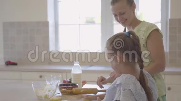 从侧面看年轻女子和她的小女儿在家里厨房做蛋糕女孩完成了工作而且很高视频的预览图