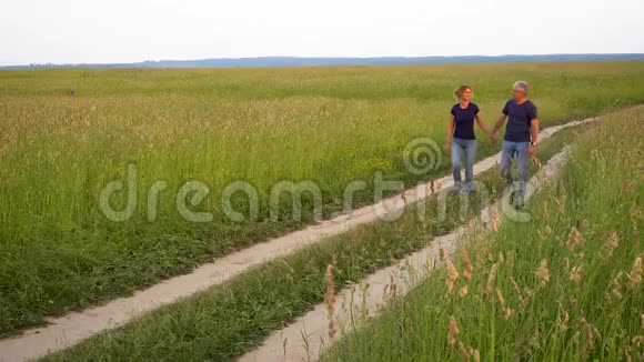 苗条的男人和女人穿着牛仔裤在田野的森林道路上在高高的绿草中在日落时欣赏大自然视频的预览图