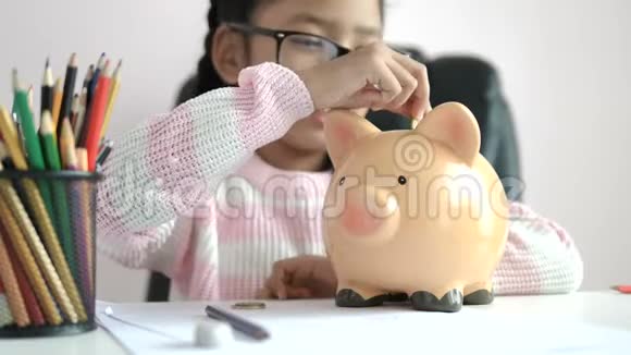 小亚洲女孩把硬币放进储蓄罐里在未来的教育中带着快乐的微笑为节省金钱而财富视频的预览图