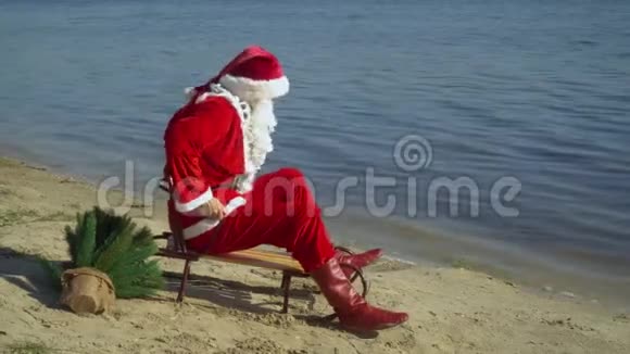 圣诞老人坐在湖沙岸上的雪橇上试图在靠近水的雪橇上前进圣诞老人视频的预览图