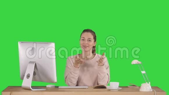 微笑的千禧一代妇女坐在办公桌前与相机交谈微笑在绿色屏幕上Chroma键视频的预览图