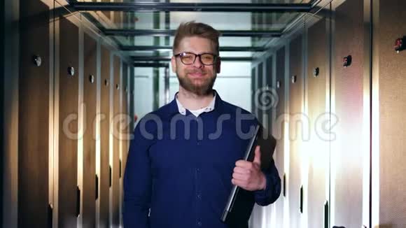 一位微笑的IT专家正拿着笔记本电脑站在服务器机房视频的预览图