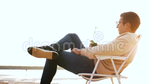 在沙滩上坐在椅子上喝啤酒的男人视频的预览图