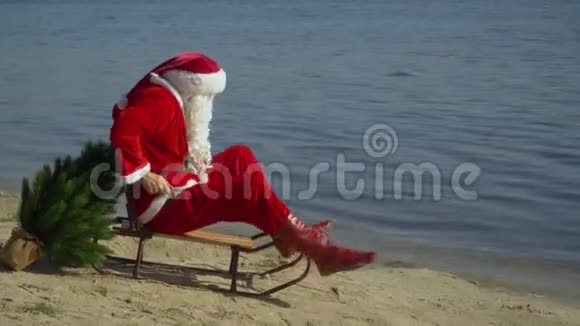 圣诞老人坐在沙滩上的雪橇上试图靠近水的雪橇前进视频的预览图