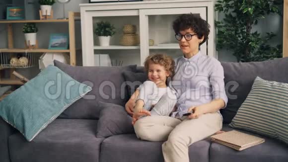 母亲和儿子一起坐在沙发上在家看电视聊天微笑视频的预览图