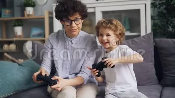 小男孩在玩电子游戏兴奋的妈妈在家拿着操纵杆视频的预览图