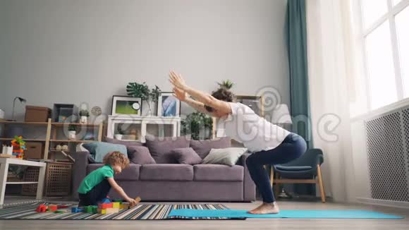 漂亮的妈妈在家做瑜伽看着儿子玩玩具视频的预览图