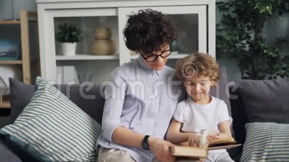 快乐的妈妈和可爱的孩子在家看沙发上的照片视频的预览图