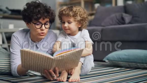 爱看书的妈妈给好奇的小男孩看书让他在光房子里的地板上放松视频的预览图