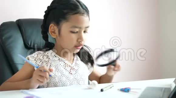 小亚洲女孩用放大镜做家庭作业用快乐微笑教育理念选择焦点浅野深度视频的预览图