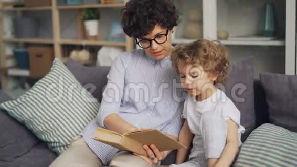 可爱的孩子和他慈爱的母亲一起看书在沙发上躺着微笑视频的预览图