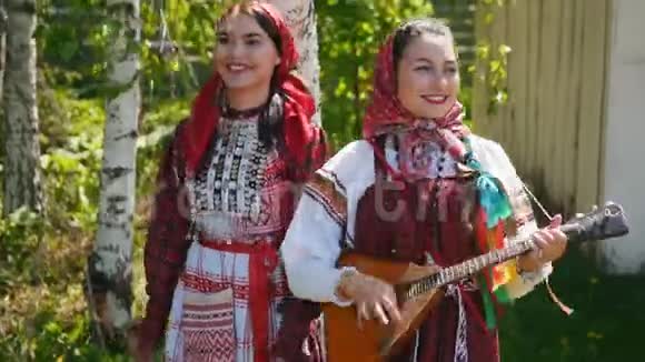 两个穿着俄罗斯传统服装的年轻女子站在桦树下跳舞视频的预览图