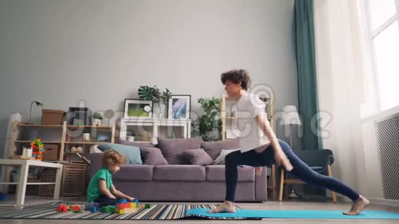 现代家庭主妇做瑜伽而她的孩子在地毯上玩积木视频的预览图
