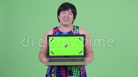 快乐年轻体重超重的亚洲女人一边说一边展示笔记本电脑视频的预览图