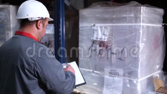 一个戴着头盔的仓库工人把他的笔记写在他的文件夹里4K慢慢视频的预览图