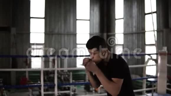 穿着黑色T恤和衬衫的男性运动员训练他的拳头移动和避免与影子对手他在热身视频的预览图