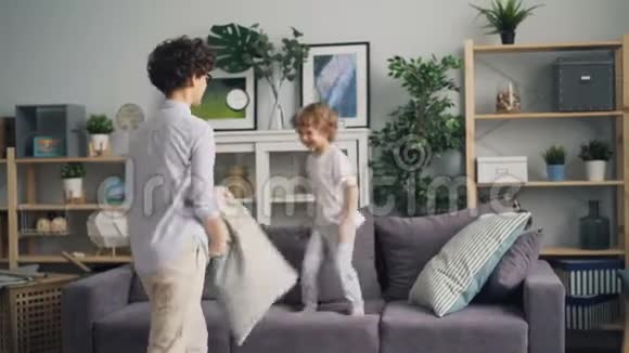 可爱的小男孩在家里和妈妈在沙发上打枕头游戏视频的预览图