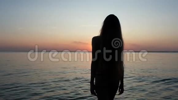 穿着泳装留着长发的剪影女孩在美丽的日落背景下视频的预览图
