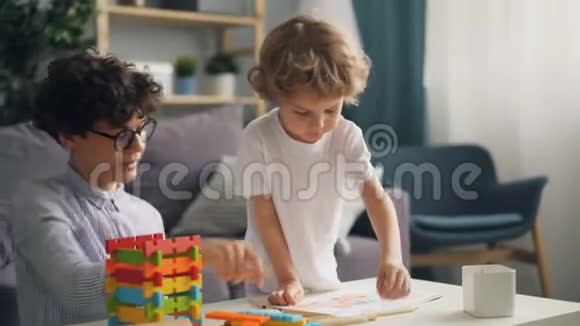小男孩和有爱心的妈妈在客厅的灯光室的桌子上画画视频的预览图
