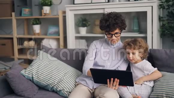 可爱的男孩在平板电脑上看动画片他有爱心的母亲拿着小玩意视频的预览图