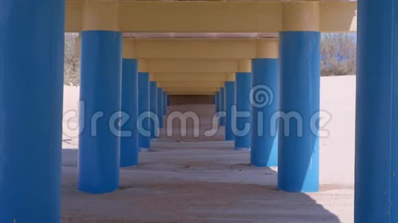 在沙滩上的桥下平行的蓝色柱子支撑着桥视频的预览图