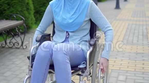 轮椅上带穆斯林头巾室外微笑的残疾青年妇女视频的预览图