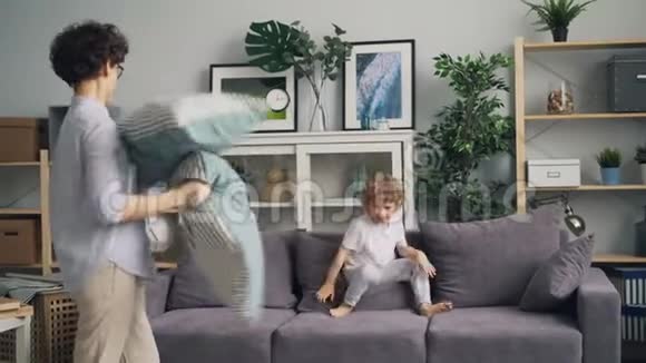 一个年轻的女人和一个小孩在沙发上扔垫子玩枕头大战视频的预览图