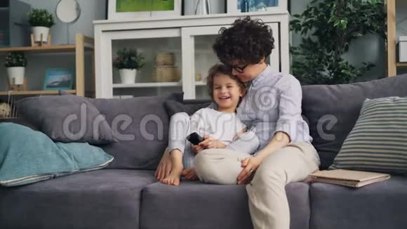 快乐的孩子和妈妈一起在家里看电视手里拿着遥控器视频的预览图