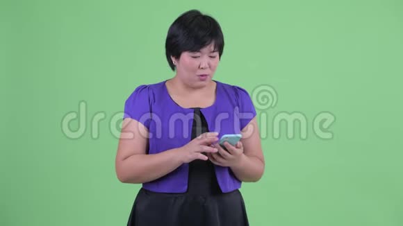 快乐的年轻超重的亚洲女人用电话得到好消息视频的预览图