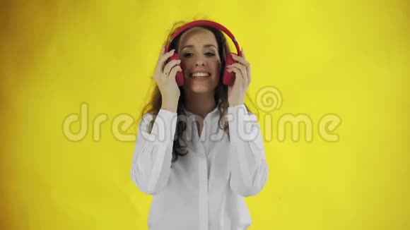 女人在黄色背景的工作室里用红色耳机听音乐视频的预览图