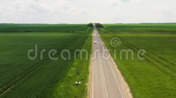 一辆白色汽车在公路上行驶在田野之间从无人机的水平射击视频的预览图