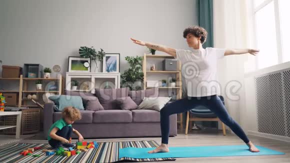 运动妈妈做瑜伽伸展身体而孩子玩积木视频的预览图