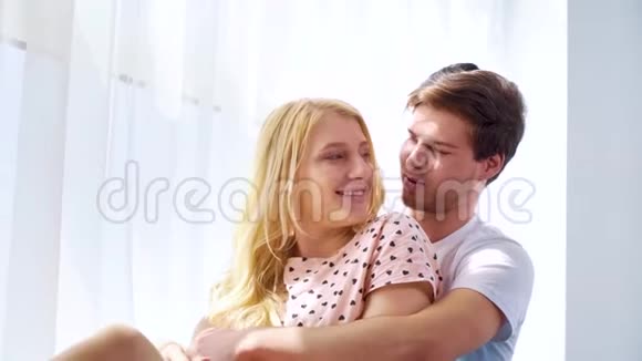 清晨阳光下一对年轻可爱的夫妇拥抱在窗帘窗前视频的预览图