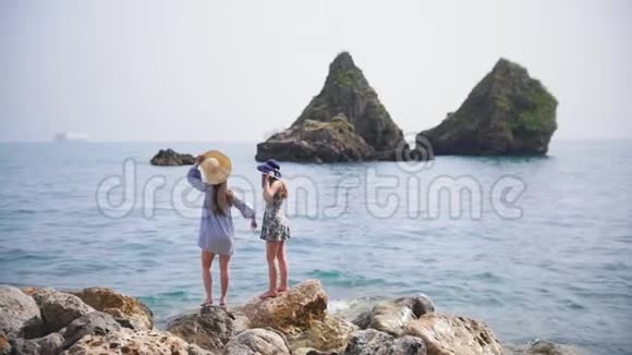 两个年轻的女人站在海中的石头上挥动手臂视频的预览图