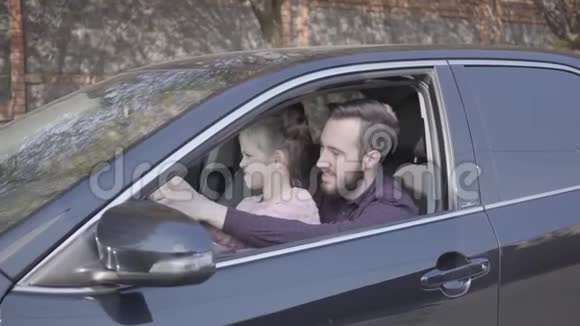 小女孩坐在爸爸的背上她坐在车里紧紧地抱着孩子正在学习开车男人和孩子表现得很大视频的预览图