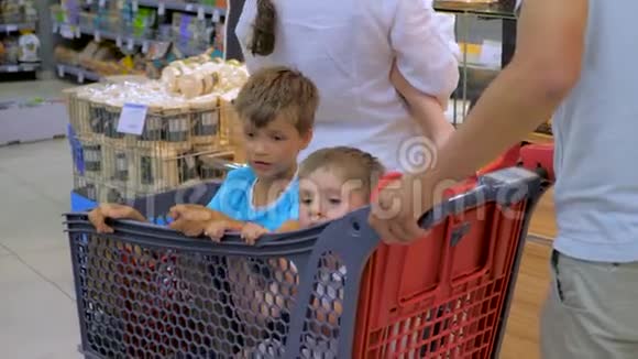 购物背景孩子们坐在购物车里父亲开着购物车进来两个孩子坐在里面视频的预览图