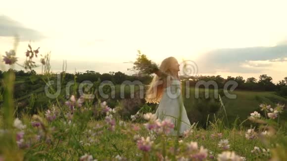 可爱的小女孩在傍晚的草地上带着野花花束旋转和跳舞视频的预览图