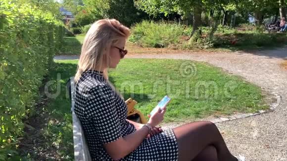 漂亮的金发女郎坐在长凳上写着电话视频的预览图