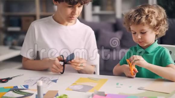 小男孩帮助他的母亲设计师在家里创作彩色纸拼贴画视频的预览图