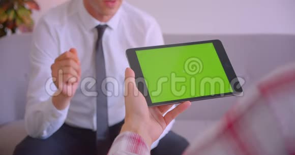 客户服务经理与客户手持平板电脑的特写肖像办公室里有绿色的彩色屏幕视频的预览图