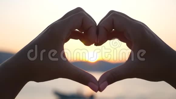 一个女人在金色的日落背景下用手把心变成自己女性手臂的轮廓显示出爱的象征视频的预览图