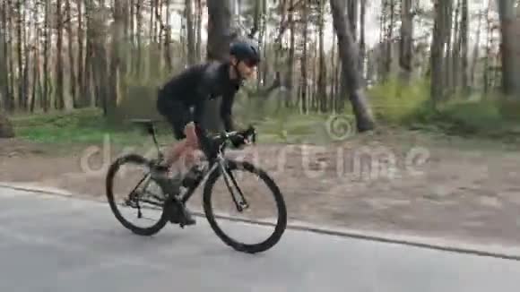 骑自行车的一侧沿着风景公园里骑着自行车穿着黑色衣服的胡子男出了马鞍踏板视频的预览图