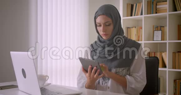 年轻迷人的穆斯林女商人戴着头巾用平板电脑拍摄特写肖像并在镜头中显示绿色屏幕视频的预览图