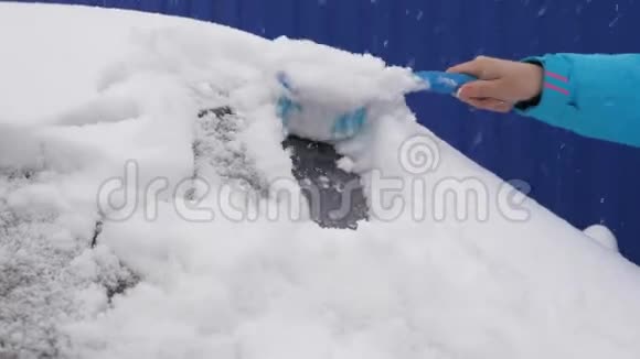 刮擦汽车挡风玻璃上的冰雪女人用刷子擦雪车大雪覆盖了汽车视频的预览图