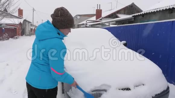 女人用刷子擦雪车刮擦汽车挡风玻璃上的冰雪大雪覆盖了汽车视频的预览图