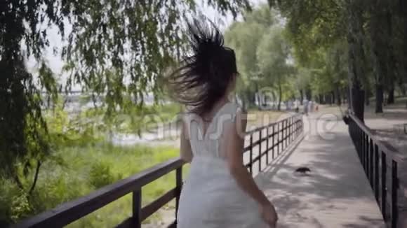 肖像迷人的年轻女孩一头黑发戴着太阳镜穿着白色的夏装穿着一件白色的长裙视频的预览图