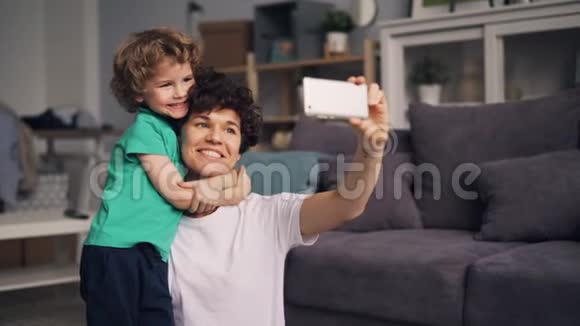 年轻女性与小男孩一起自拍用智能手机亲吻和拥抱视频的预览图