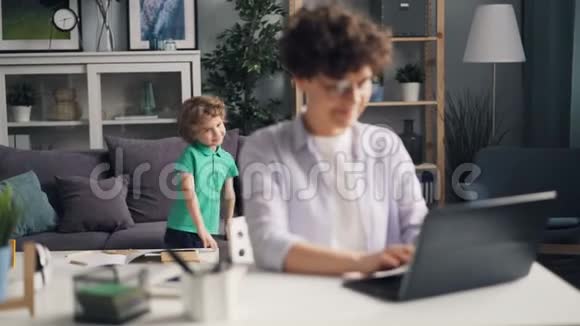 女孩用笔记本电脑工作然后和儿子聊天亲吻他玩视频的预览图